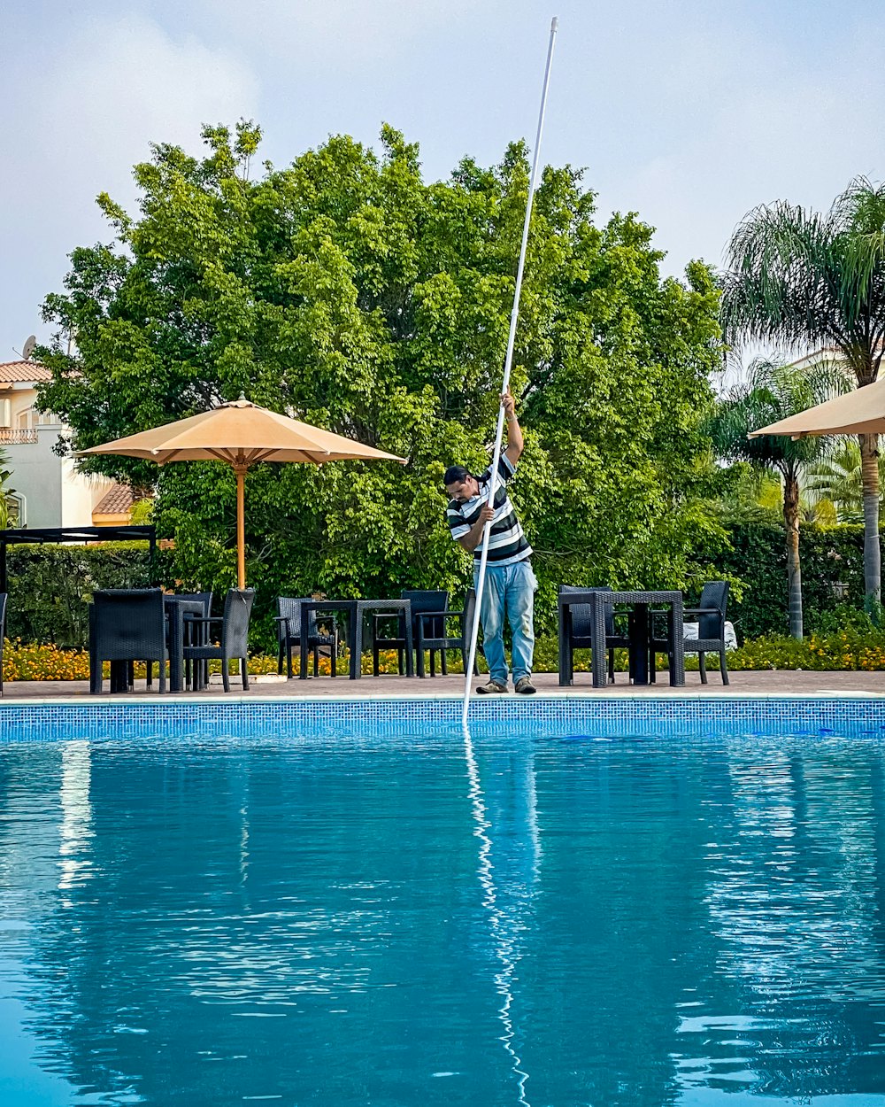 A pool technician reaching out over a backyard pool with a long-handled cleaning pole.