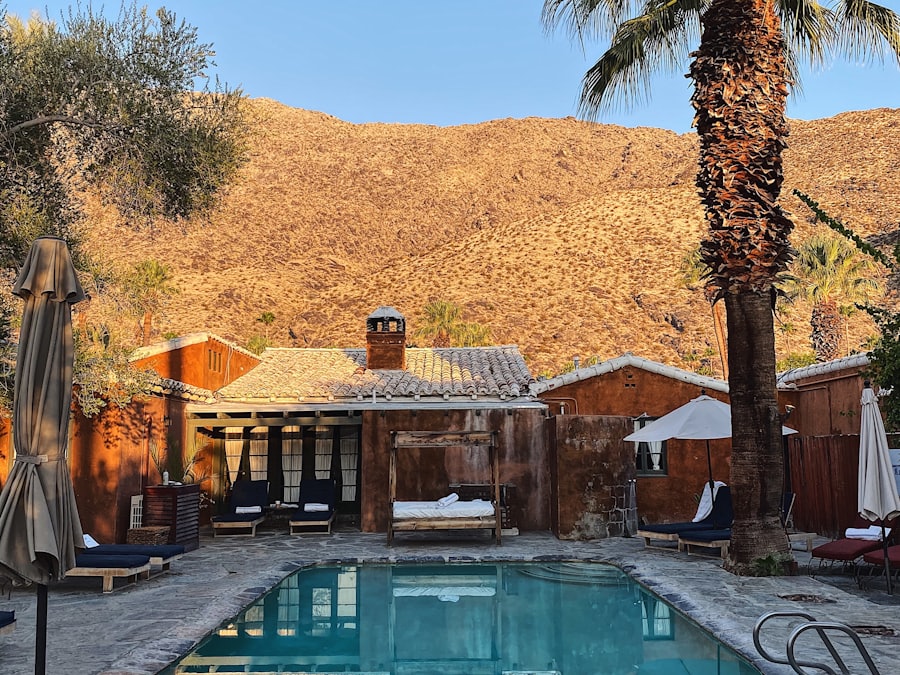 Poolside chairs and a shaded cabana with bare desert hills rising behind.